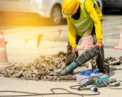 Male,worker,with,safety,equipments,drilling,concrete,repairing,driveway,surface